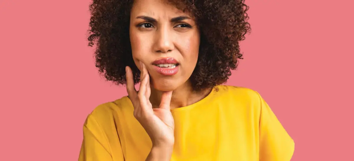 Mulher sentindo desconforto na bochecha mostrando sintomas de boqueira