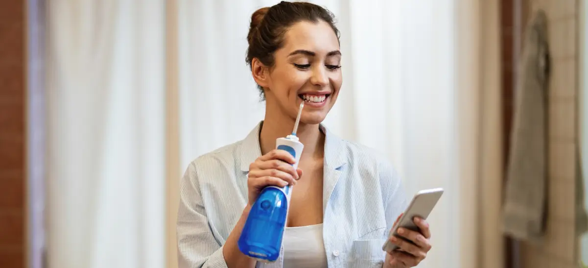 Jovem feliz escovando o dente utilizando uma escova de dente elétrica