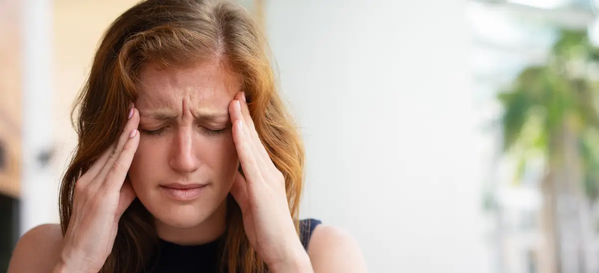 Mulher com dor intensa no rosto segurando a lateral da cabeça, sintoma típico da neuralgia do trigêmeo