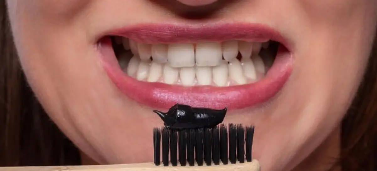 Mulher colocando pasta de dente com carvão ativado na escova de dentes