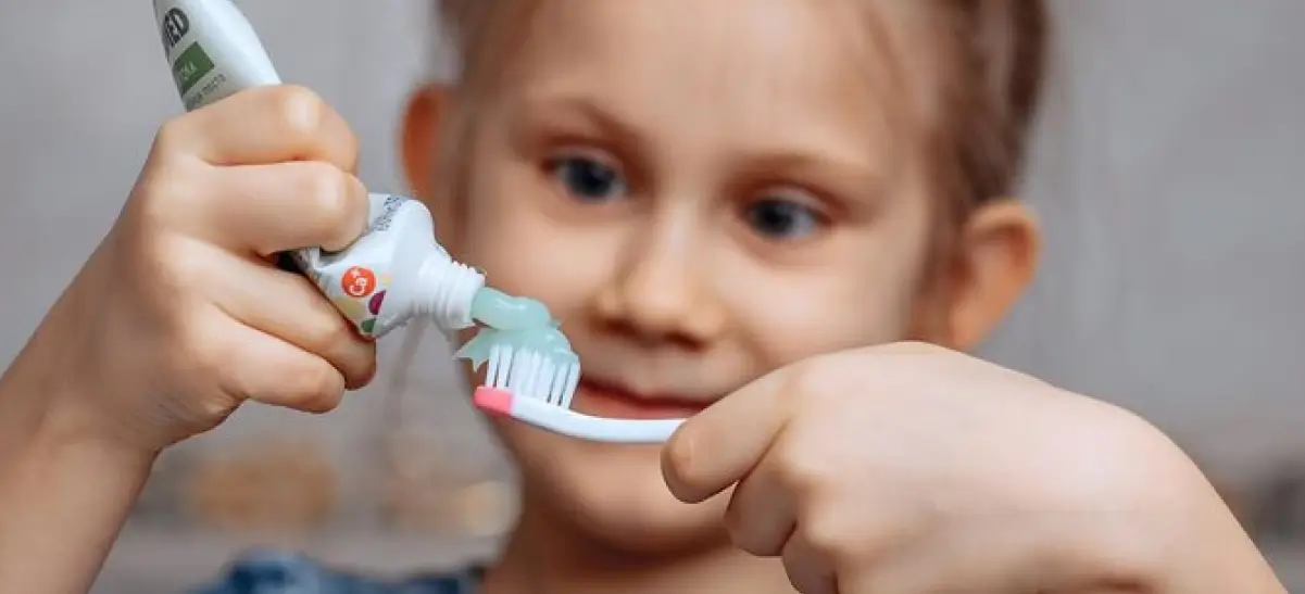 Criança aplicando pasta de dente infantil na escova antes de escovar os dentes