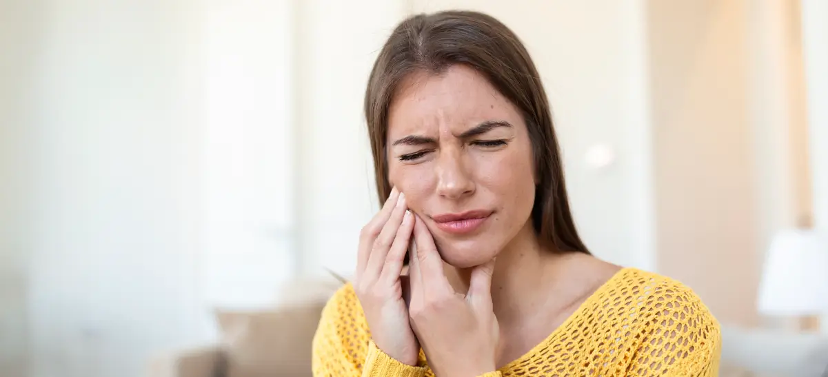 Mulher com dor de dente segurando o rosto, representando sintomas relacionados a odontoma